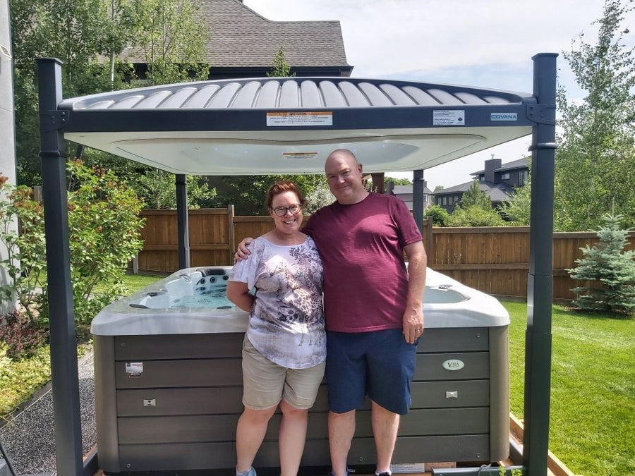 A couple beside their hot tub with its cover raised