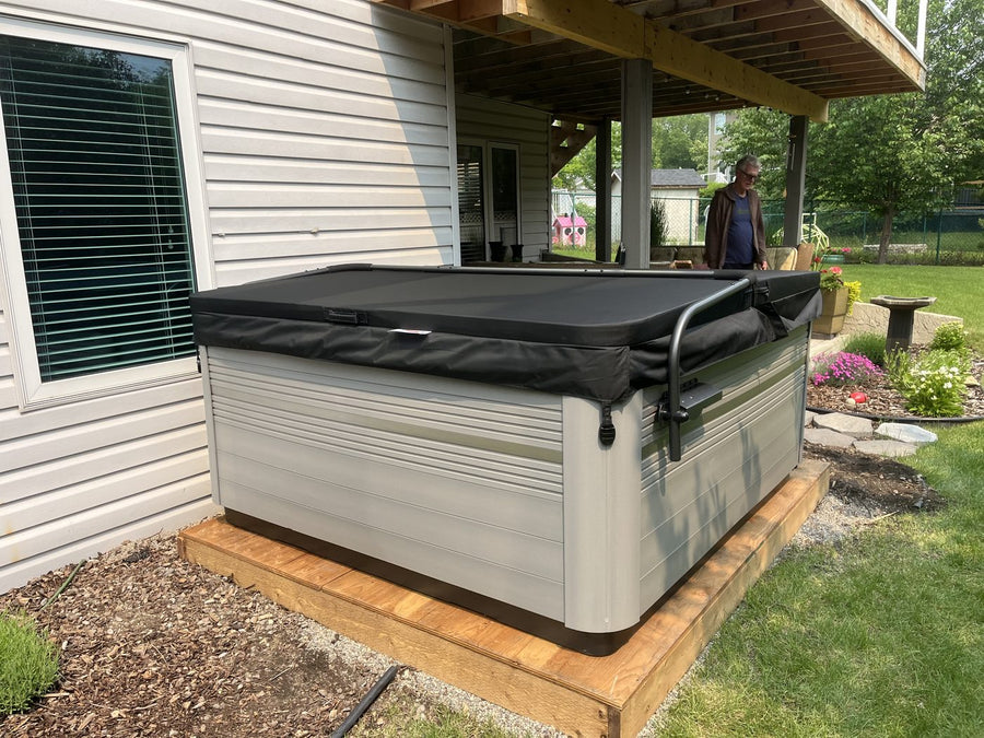 A hot tub installed on a low deck beside a house and a mulch garden bed