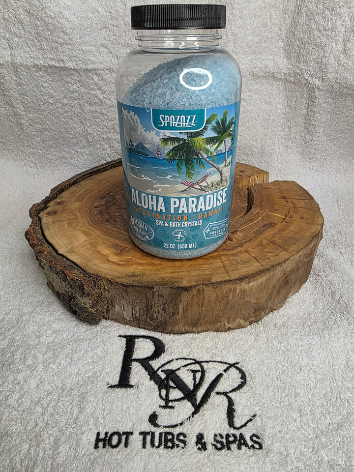 Bottle of Aloha Paradise aromatherapy crystals on a wooden block with RnR Hot Tubs & Spas branding in the background.