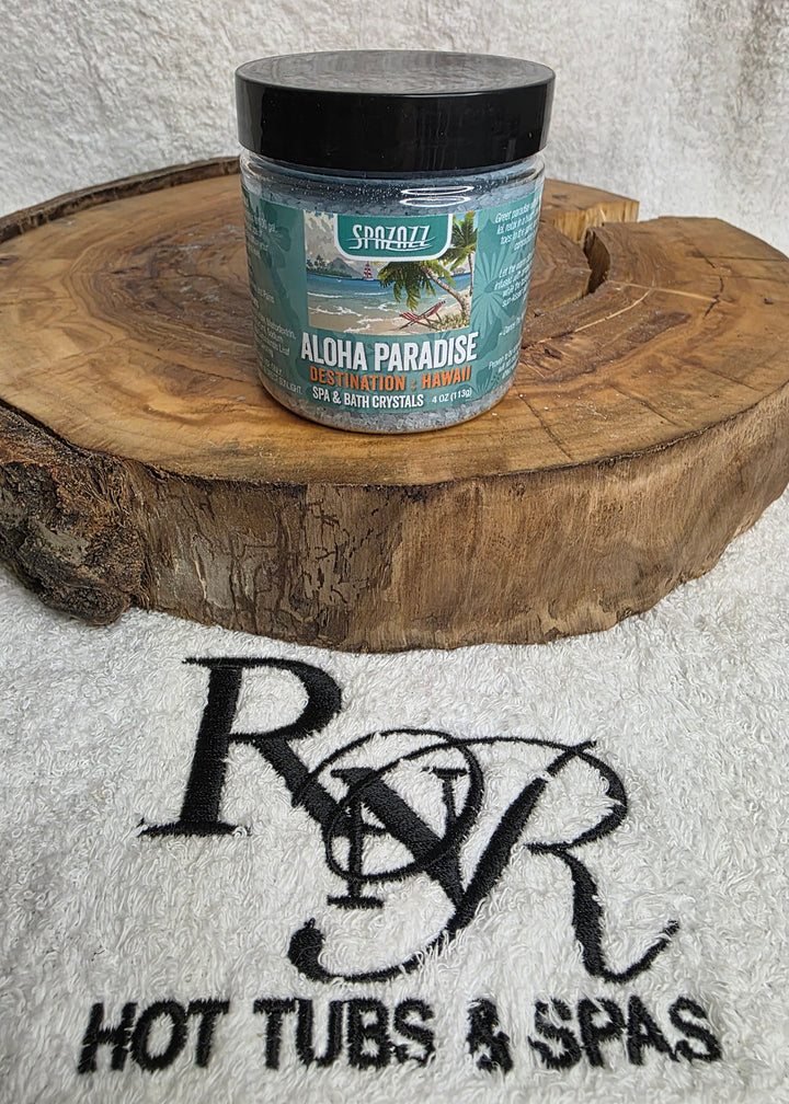 Container of Aloha Paradise aromatherapy crysals on a wooden block with RnR Hot Tubs & Spas branding in the background.