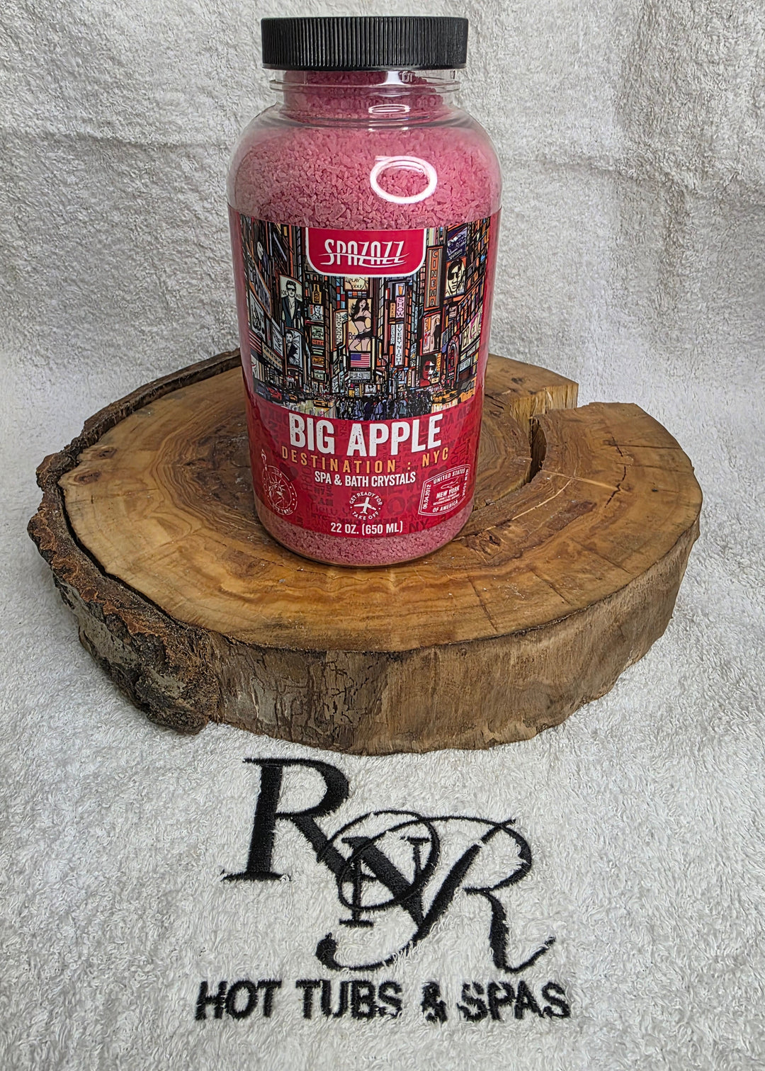Bottle of Big Apple Squeeze on a wooden block with RnR Hot Tubs & Spas branding in the background.