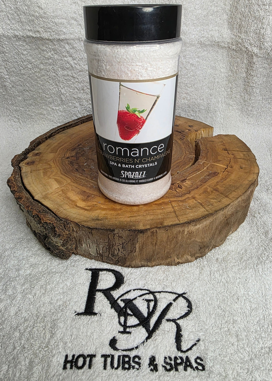 Bottle of Spazazz Romance aromatherapy crystals on a wooden block with RnR Hot Tubs &amp; Spas logo in the background.