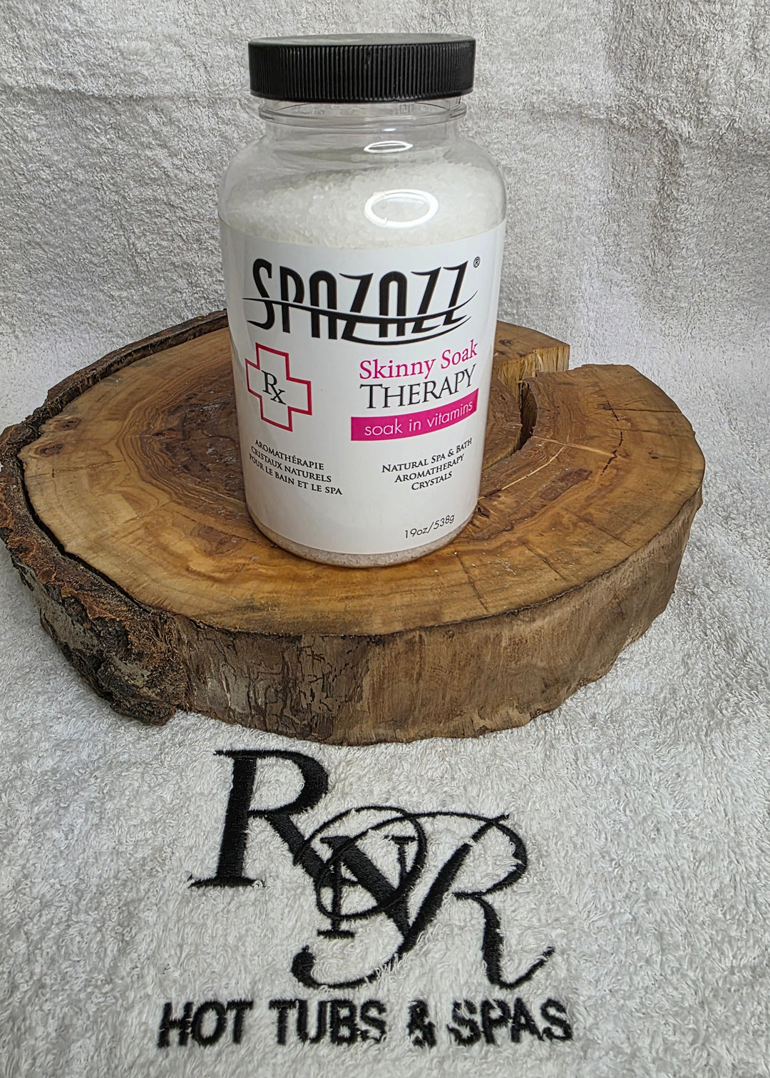 Bottle of Spazazz Skinny Soak aromatherapy crystals on a wooden block with RnR Hot Tubs &amp; Spas logo in the background