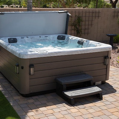 A filled hot tub with the cover lifted clear, moulded seating visible, and steps at one corner