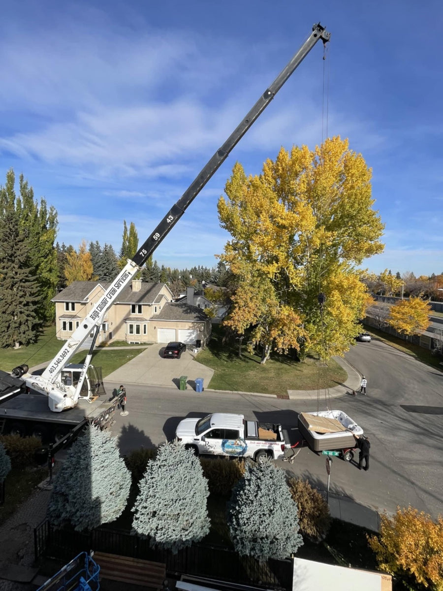 A crane lifting a hot tub over a house into the backyard