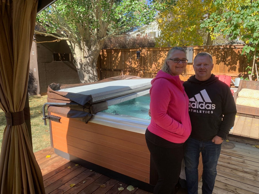 A couple beside their swim spa on a backyard deck