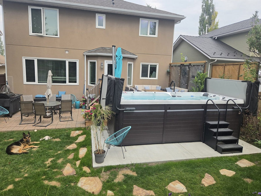 A swim spa installed on a concrete pad in a landscaped backyard, beside a family home