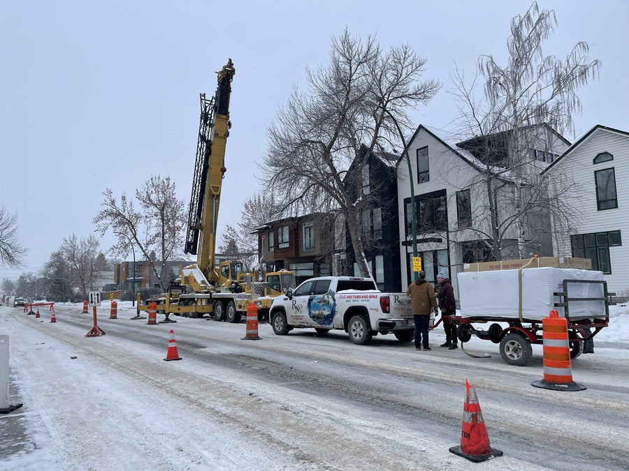 A crane and the RnR truck and trailer on a snowy Calgary street, moving a hot tub